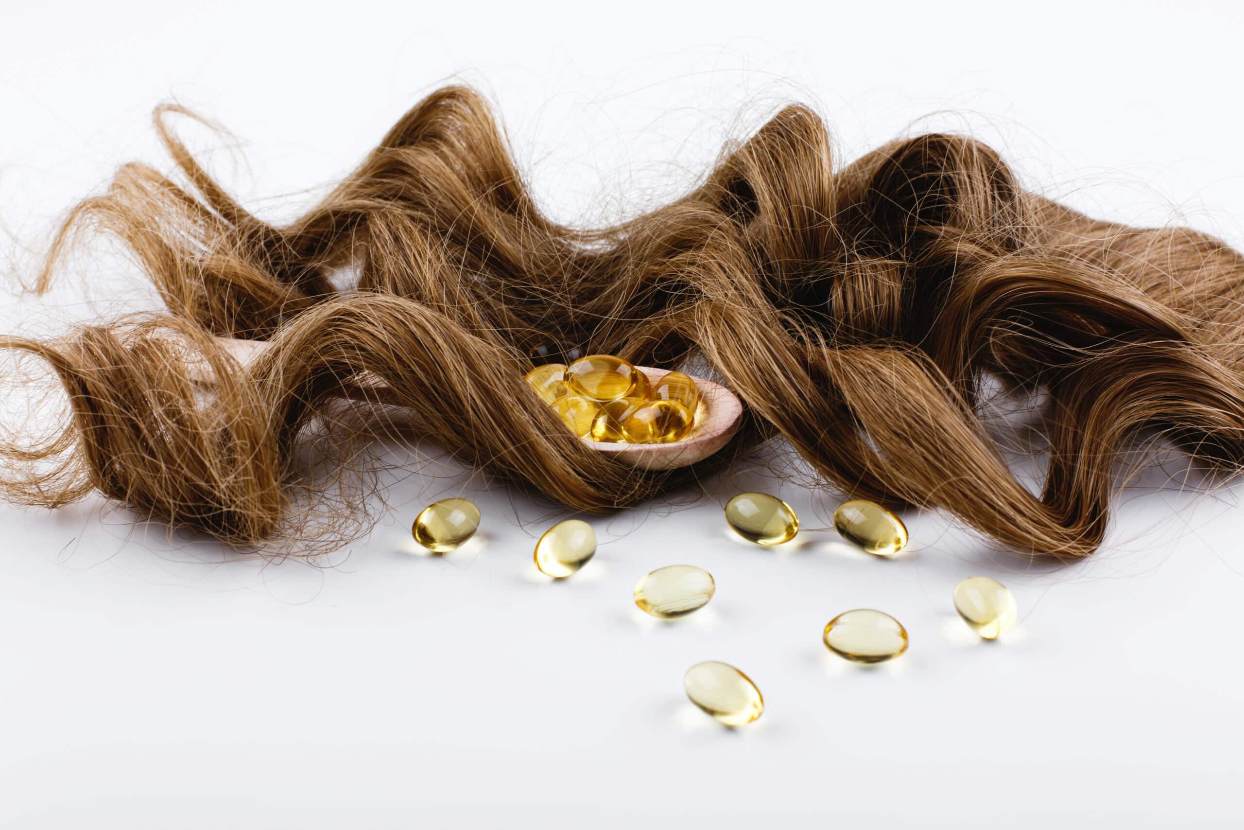 vitamin oil capsules on white background next to a lock of brown hair
