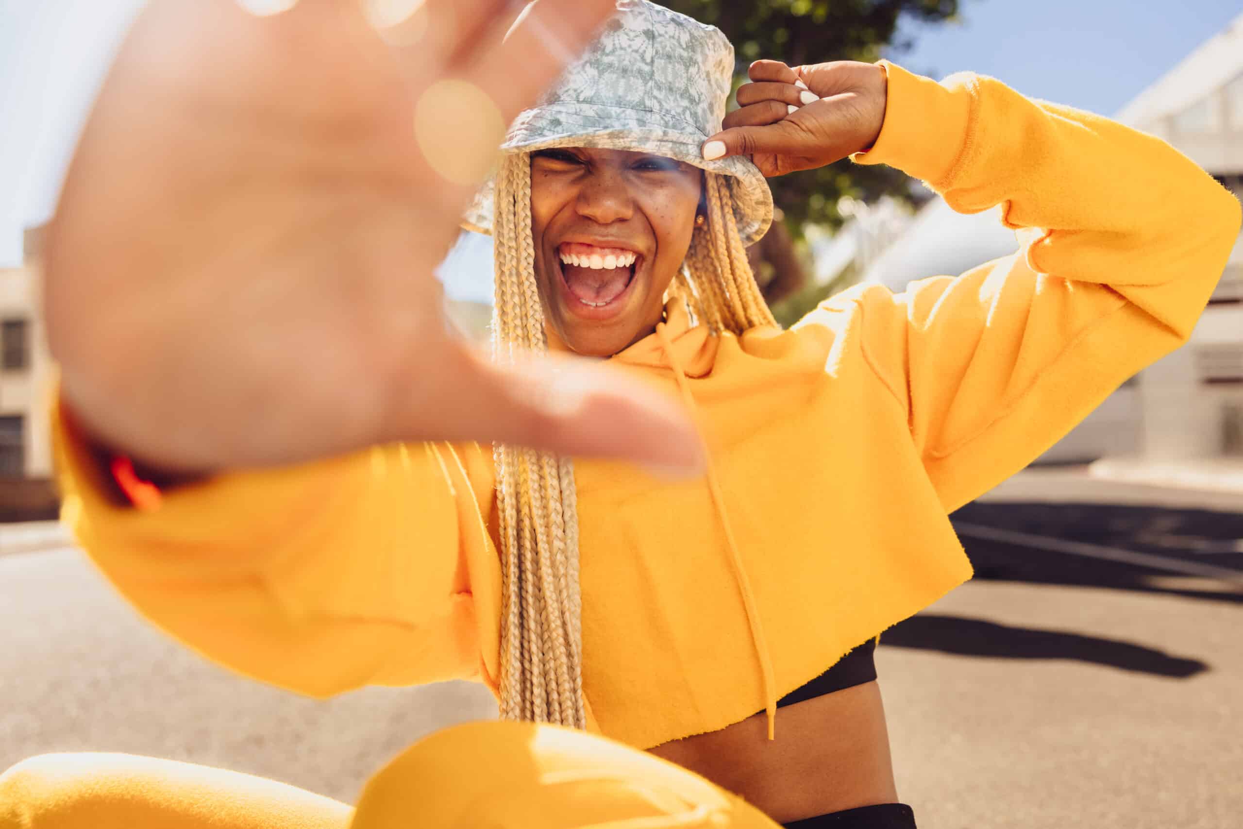 young woman with long braided hair smiling and holding up one hand blocking part of the camera's view