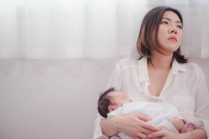 tired woman with black hair holding newborn baby