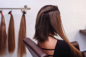 a woman is turned away sitting in a chair getting brown hair extensions put in