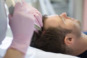 gloved hands shining a red laser medical device on a man's parted hair