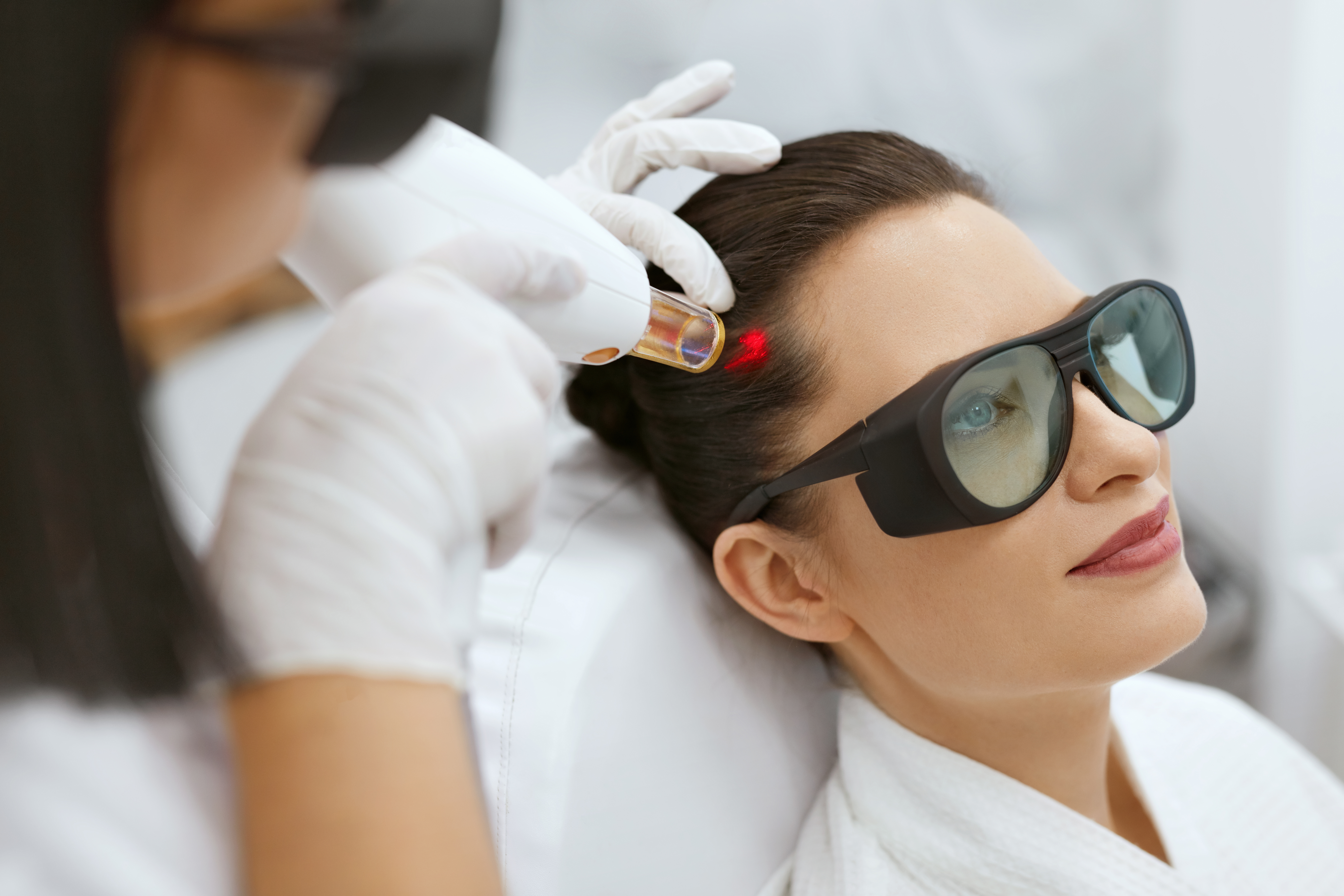 smiling women in medical sunglasses is receiving red laser therapy on her hair part
