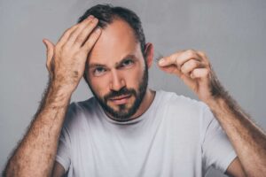 bearded middle aged man looking in mirror at his receding hairline