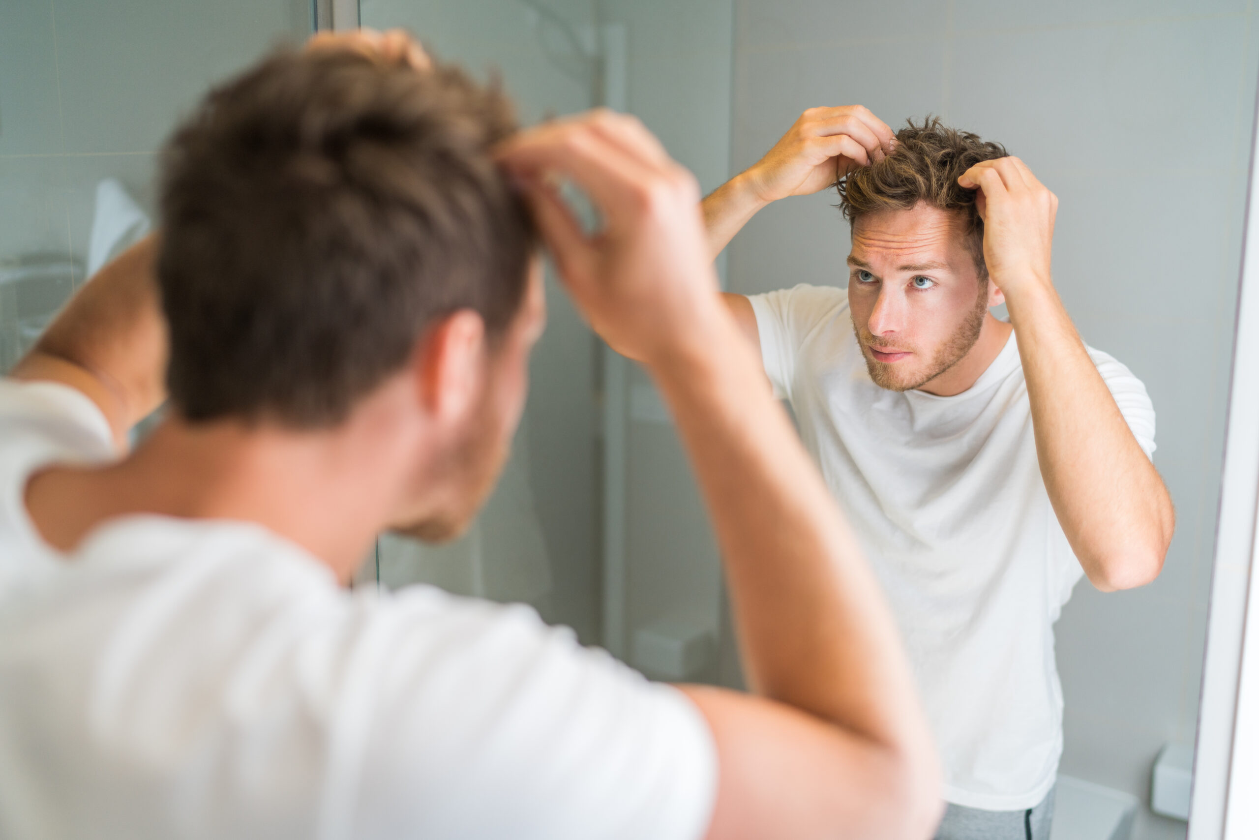 young man looking into mirror examining his hairline for hair loss
