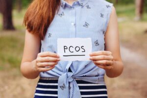 woman holding a handwritten paper sign that says PCOS