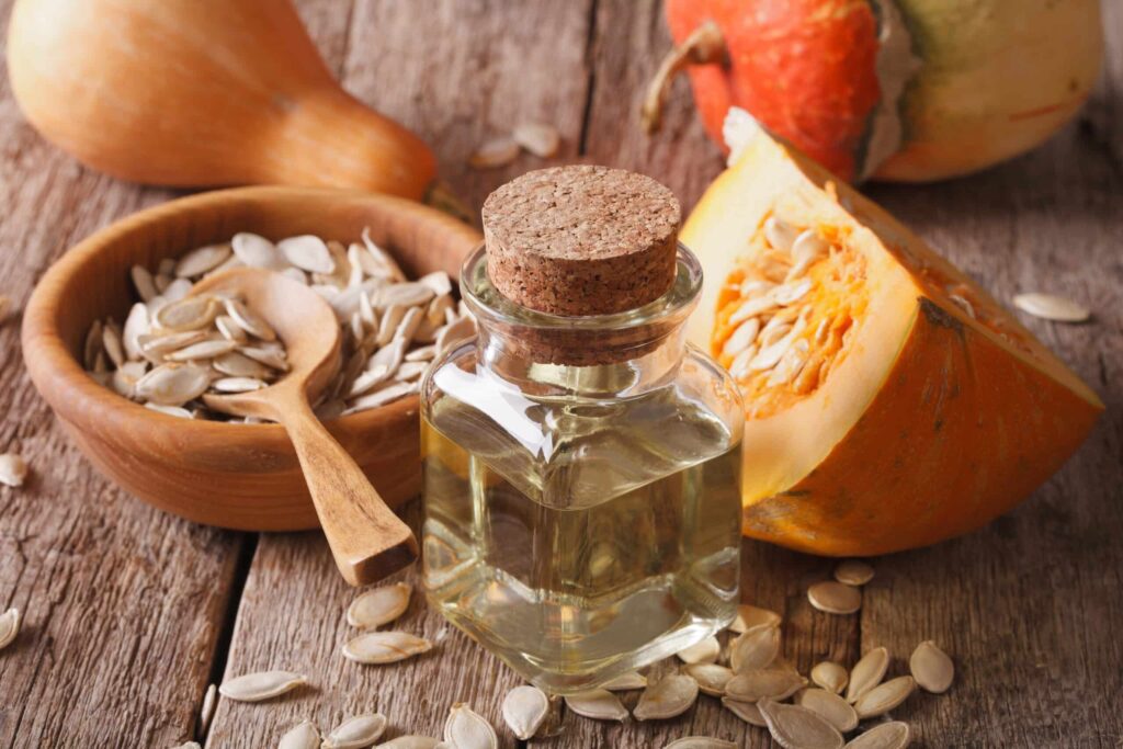 photo of table with pumpkin seeds in a bowl, a slice of pumpkin, and a jar of pumpkin seed oil
