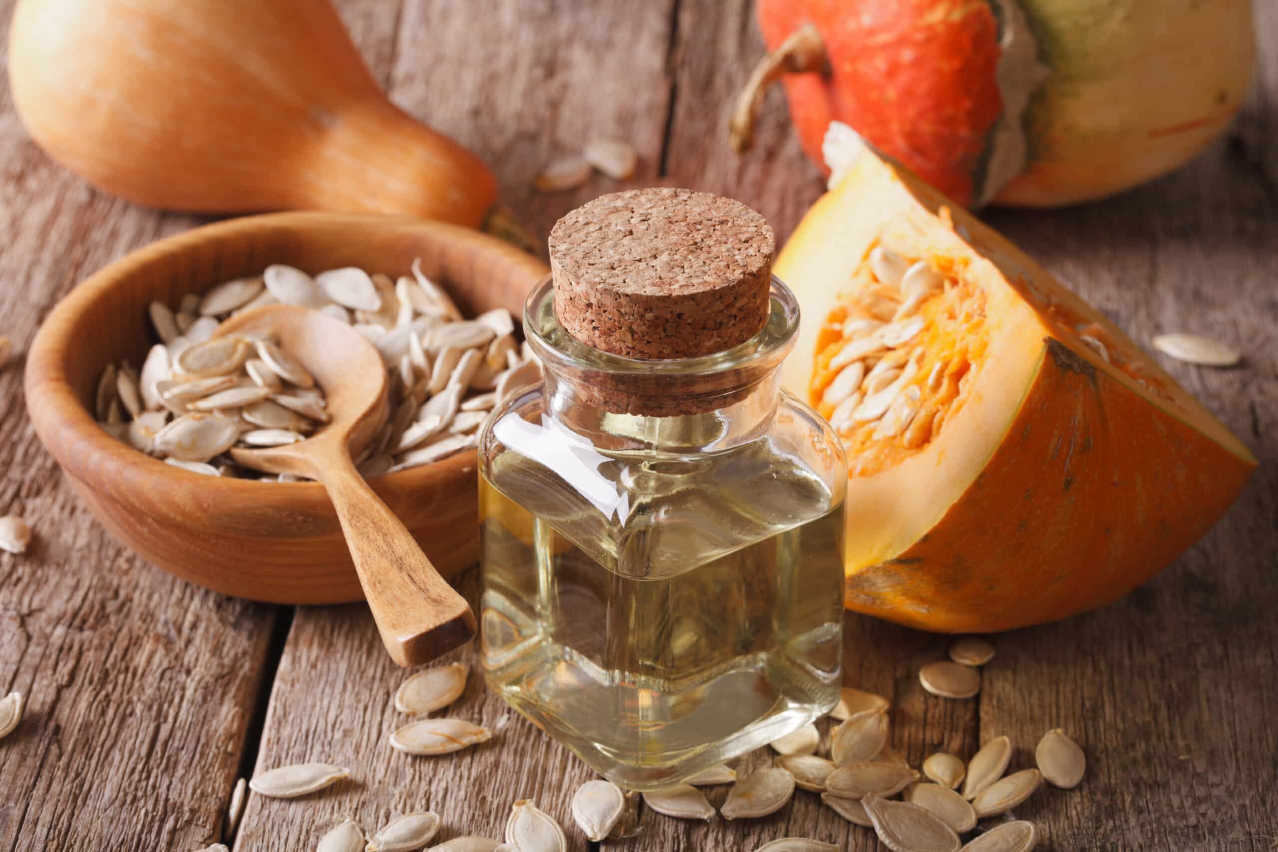 photo of table with pumpkin seeds in a bowl, a slice of pumpkin, and a jar of pumpkin seed oil