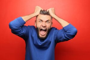 man grabbing his hair and yelling angerly on a red background