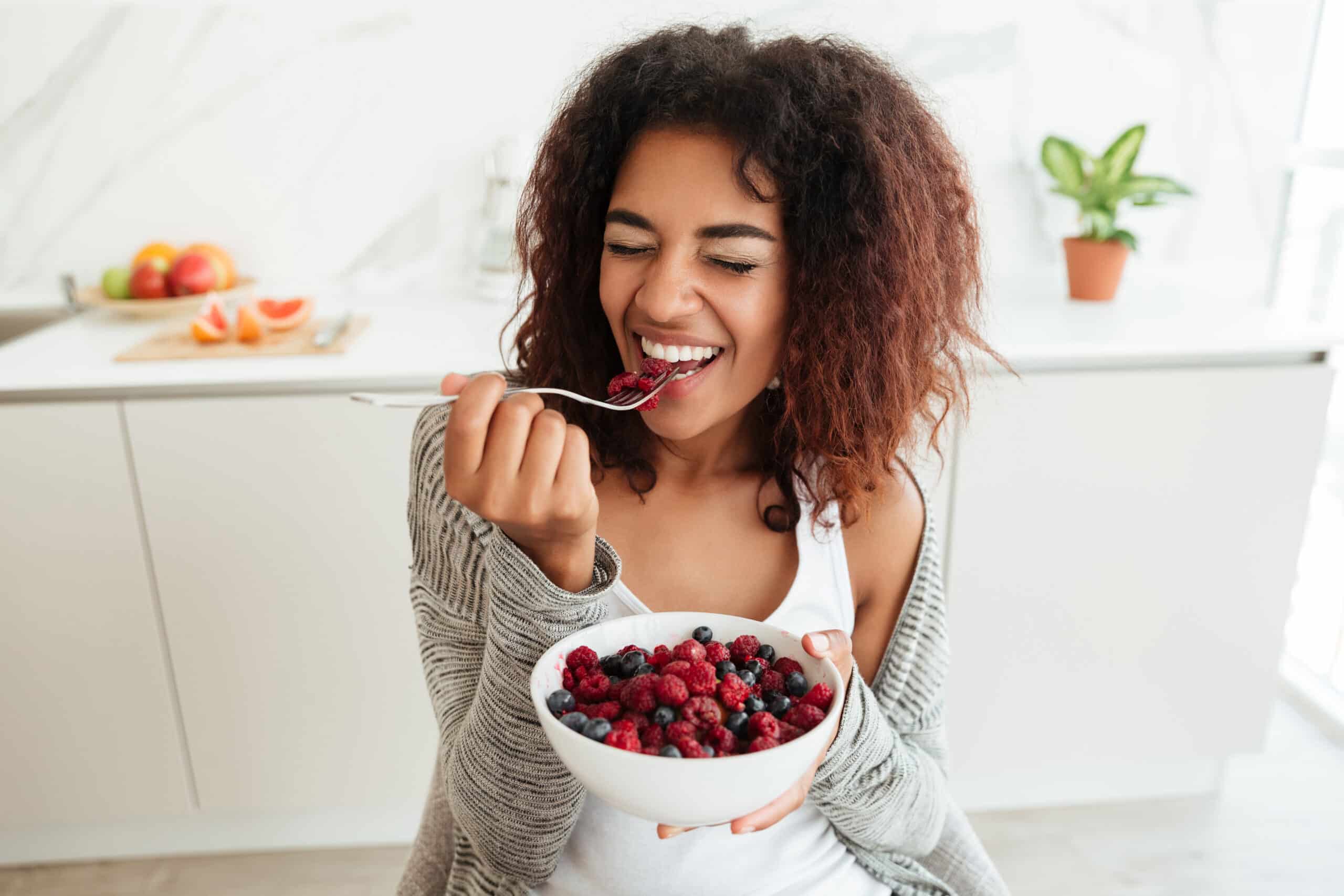 smiling young woman with curly hair eating a bowl of berries