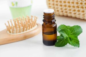 small bottle of essential oil on a white table next to peppermint leaves and a comb