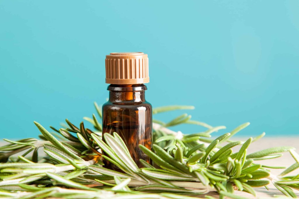 bottle of essential oil sitting on a table next to rosemary leaves on a blue background