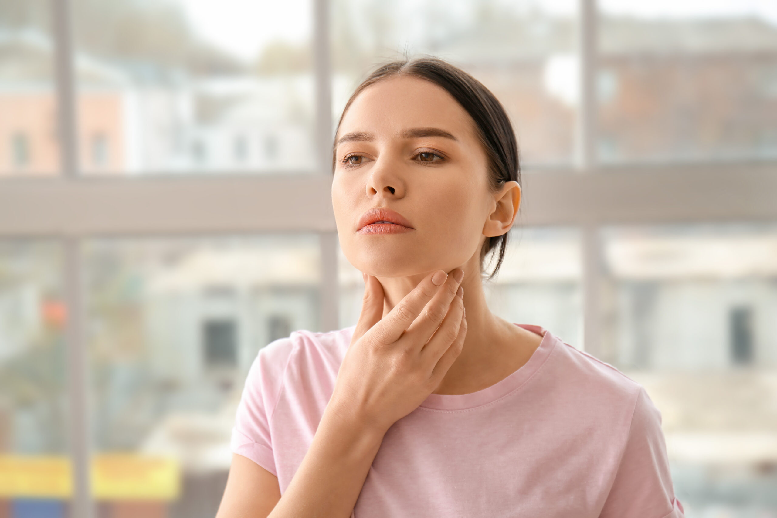 distressed woman holding her thyroid on her neck