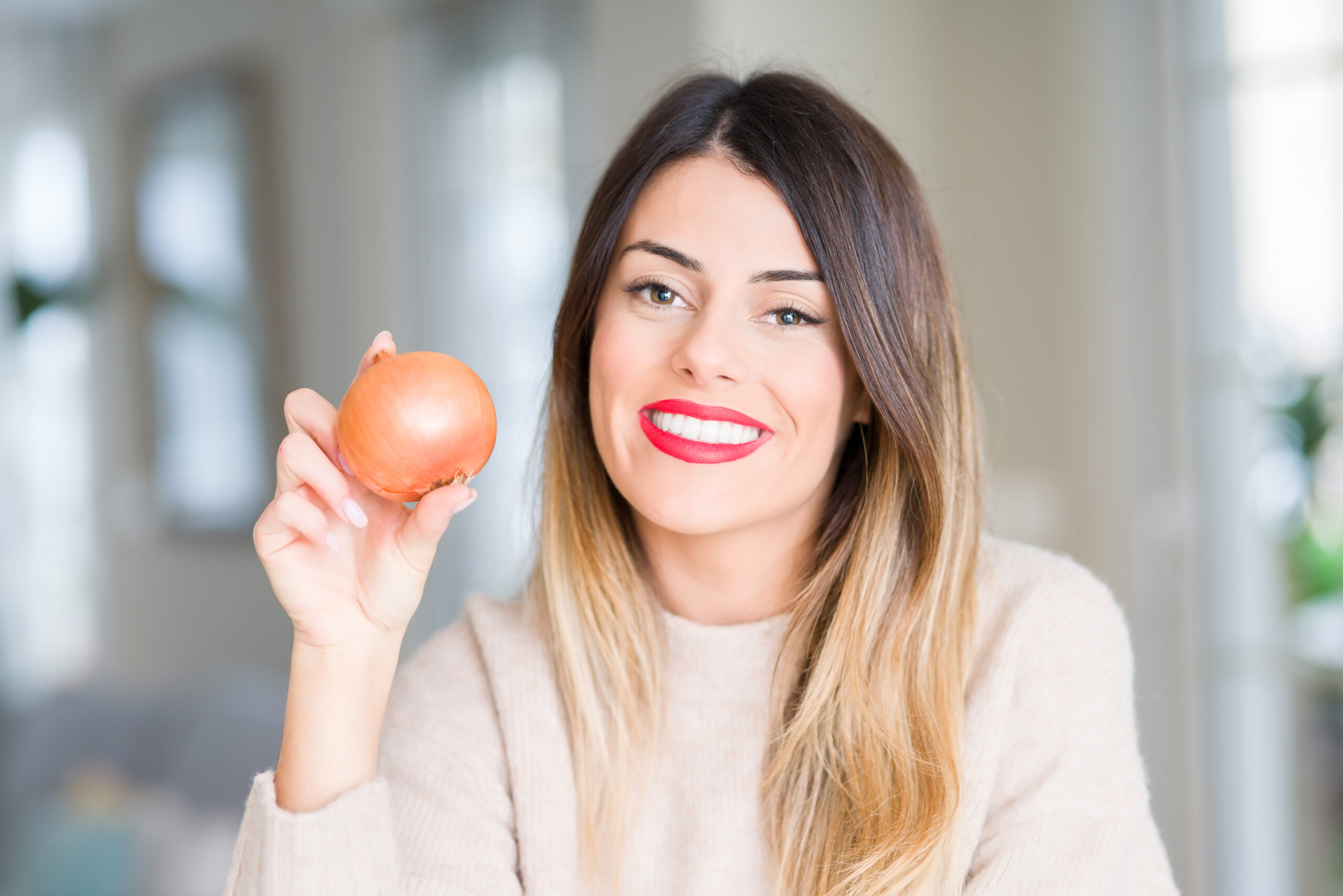 Smiling woman with pretty long hair holding an onion and looking into the camera